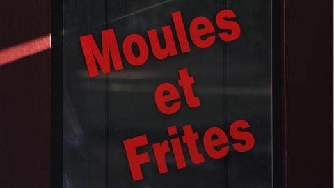 Ein schwarzes Schild auf dem Moules et Frites in roten Buchstaben geschrieben ist.