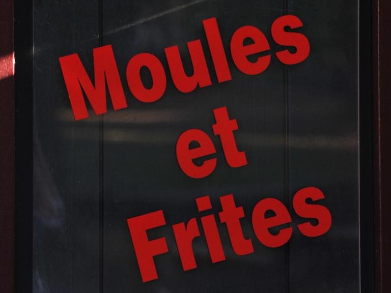 Ein schwarzes Schild auf dem Moules et Frites in roten Buchstaben geschrieben ist.
