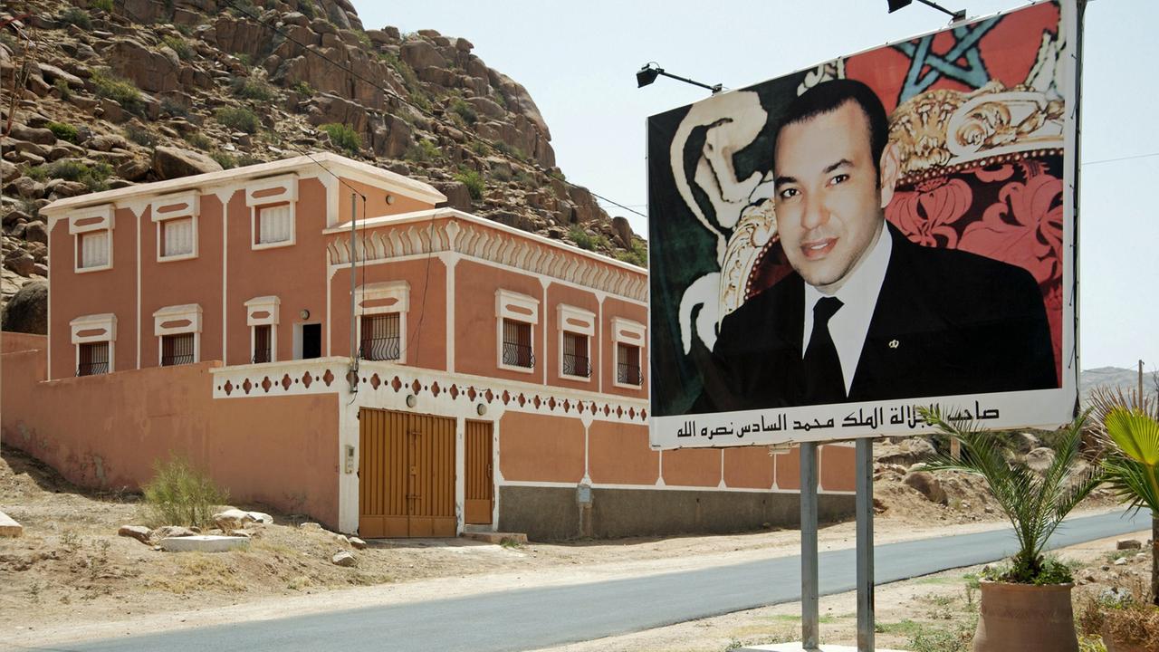 Plakat mit dem Porträt des marokkanischen Königs Mohammed VI. an einer Straße, dahinter ist ein Haus zu sehen.