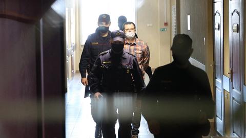 Ein Mann wird durch einen Flur von mehreren Polizisten vor Gericht geführt.