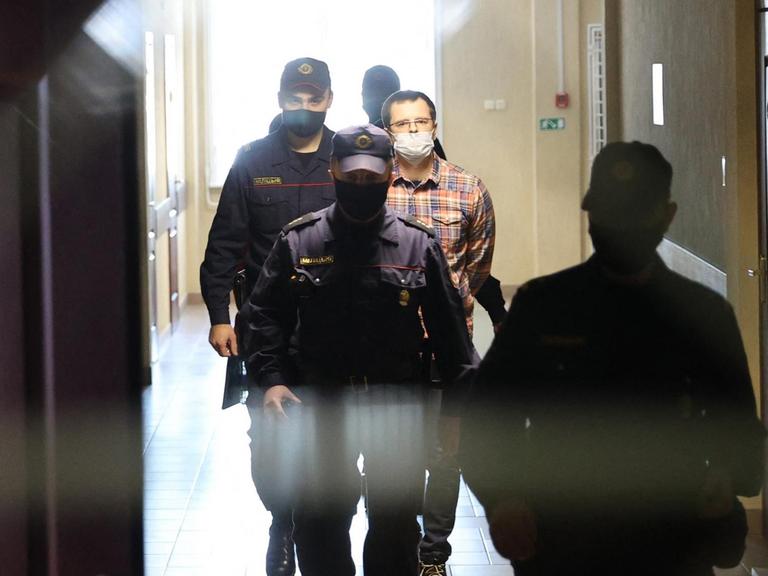 Ein Mann wird durch einen Flur von mehreren Polizisten vor Gericht geführt.