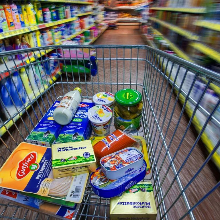 Ein Einkaufswagen mit Lebensmitteln wird zwischen Regalen geschoben.