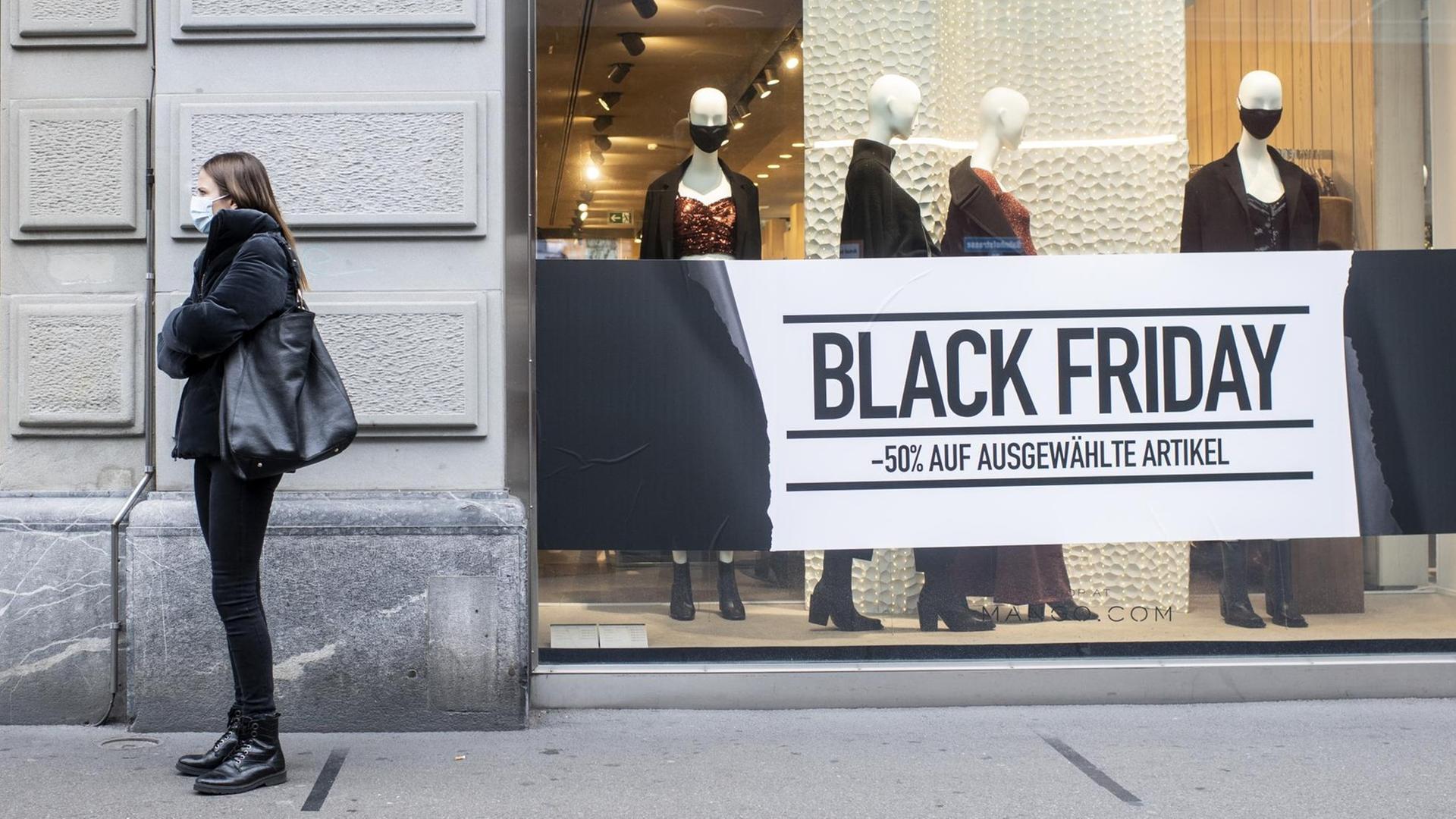 Eine Frau steht mit Maske vor einem Schaufenster, das für den "Black Friday" geschmückt ist.