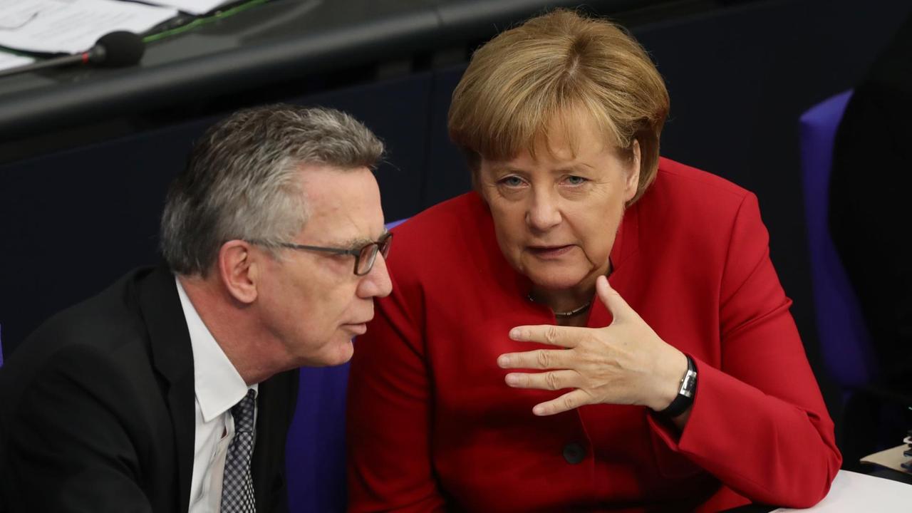Bundeskanzlerin Angela Merkel und Bundesinnenminister Thomas de Maiziere (beide CDU) unterhalten sich im Bundestag.