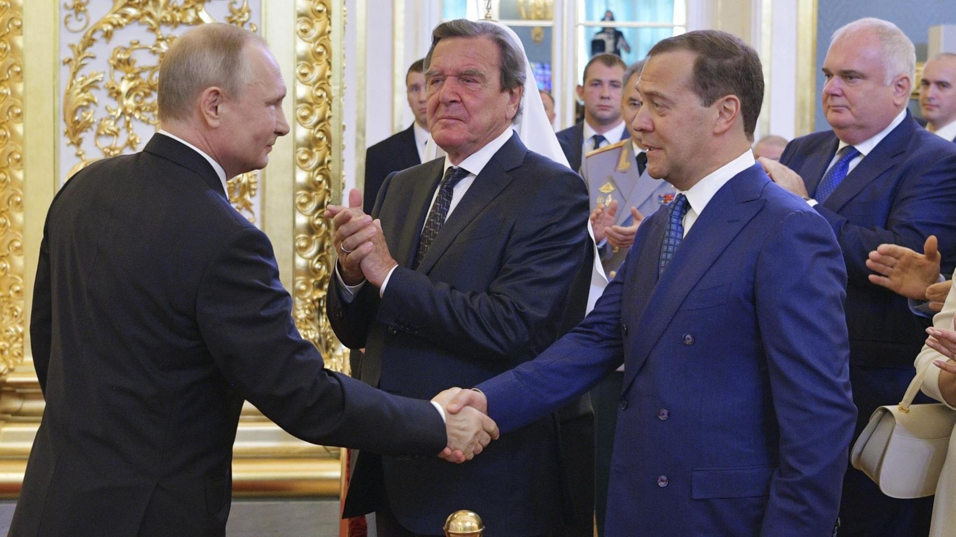 Wladimir Putin gibt Dimitri Medwedew, Minister-Präsident von Russland, die Hand. Gerhard Schröder steht neben den beiden. Wladimir Putin gibt Dimitri Medwedew, Minister-Präsident von Russland, die Hand. Gerhard Schröder steht neben den beiden.