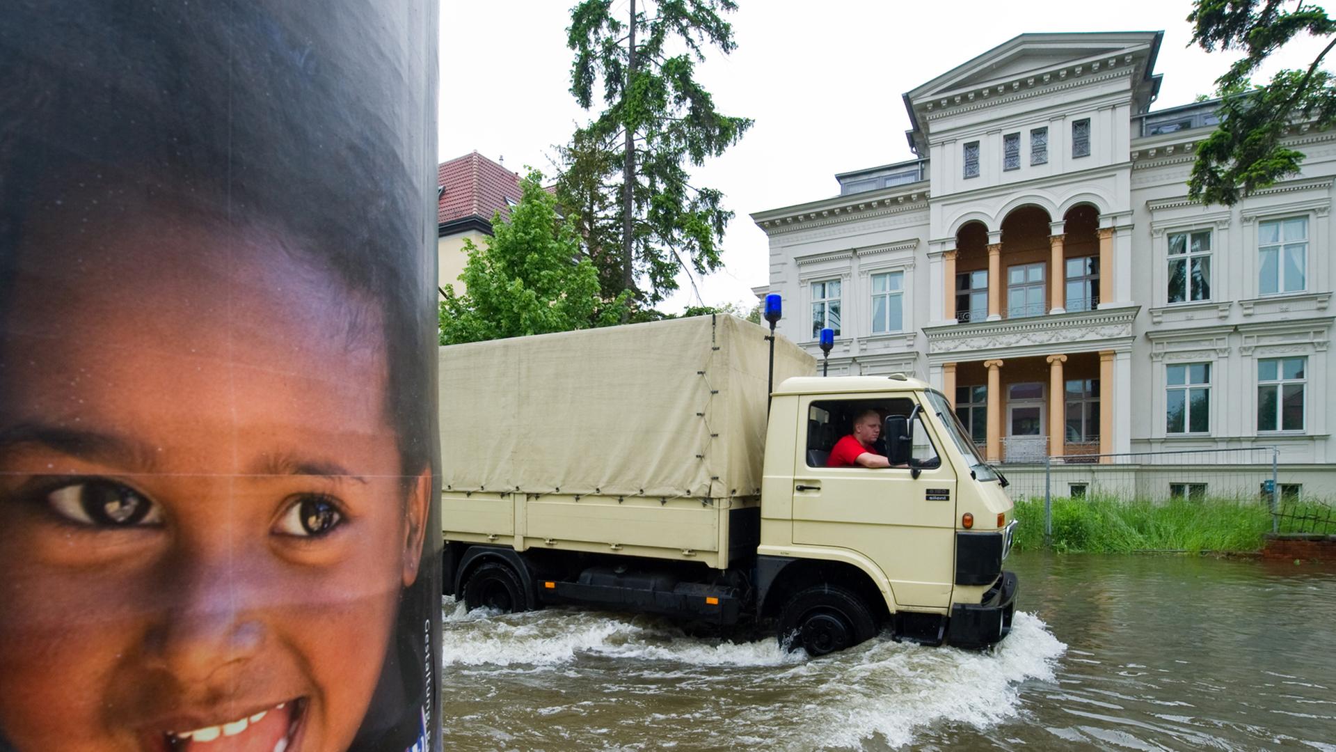 Ein Lkw des Deutschen Roten Kreuz fährt an einem Plakat mit einem lachenden Kind im vom Oder-Hochwasser überfuteten Buschmühlenweg in Frankfurt (Oder) vorbei.