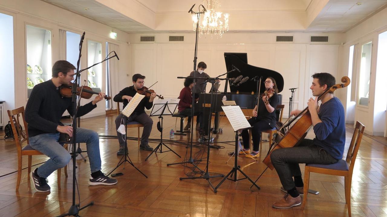 Fünf Musiker an ihren Streichinstrumenten und am Flügel zwischen Mikrofonen in einem Festsaal mit Parkettboden.