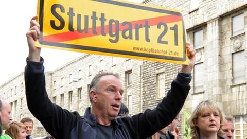 Stuttgart 21-Gegner demonstrieren in Stuttgart vor einem Bautor, im Hintergrund ist der Südflügel des Hauptbahnhofes zu sehen.