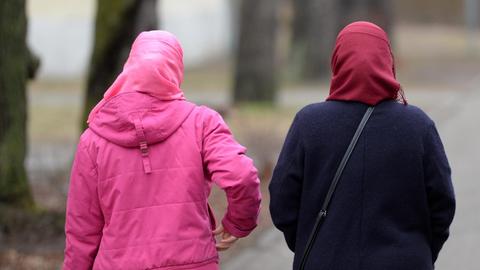 Man sieht zwei Frauen mit Kopftuch von hinten auf einer Allee.