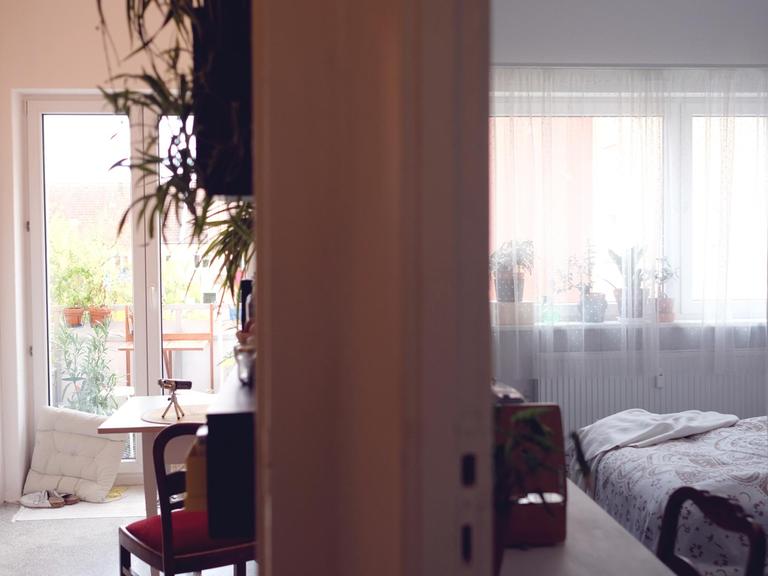 Ein Blick in zwei Räume. Links von der trennenden Wand ist die Küche mit angrenzendem Balkon zu sehen. Rechts das Schlafzimmer.
