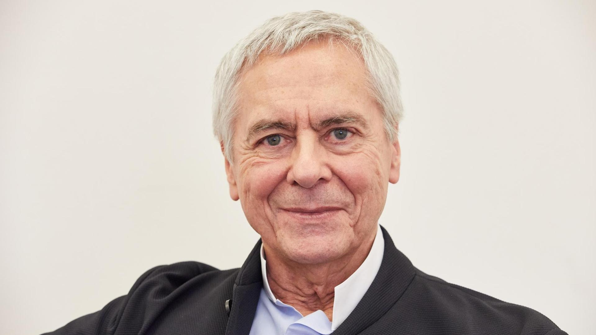 Porträt des Ballettintendanten und Chefchoreografen John Neumeier, vor einer weißen Wand.