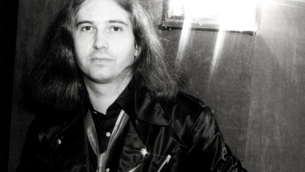Jim Steinman lehnt an einer Wand, trägt Lederjacke und eine lederne Krawatte (Schwarz-Weiß-Fotografie)