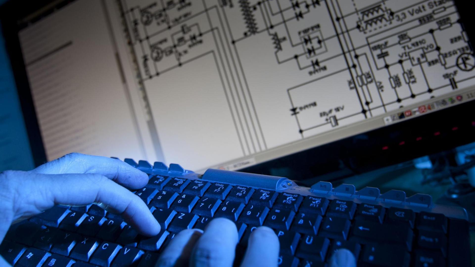 Ein Mann tippt auf einer Computer-Tastatur vor einem elektrischen Schaltplan.