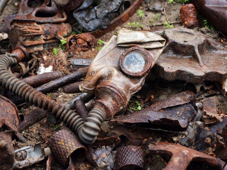 Überbleibsel einer Gasmaske und andere verrostete Metallteile aus dem Zweiten Weltkrieg liegen auf dem Boden.