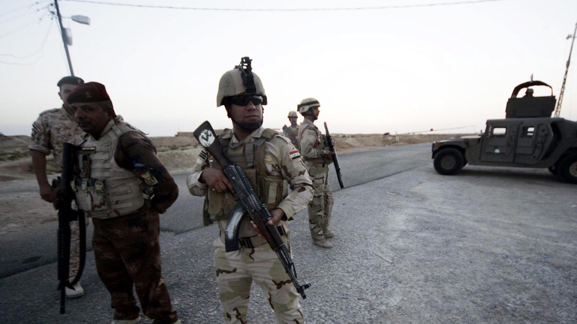 Vor einem Militärfahrzeug stehen vier Soldaten mit Maschinengewehren.