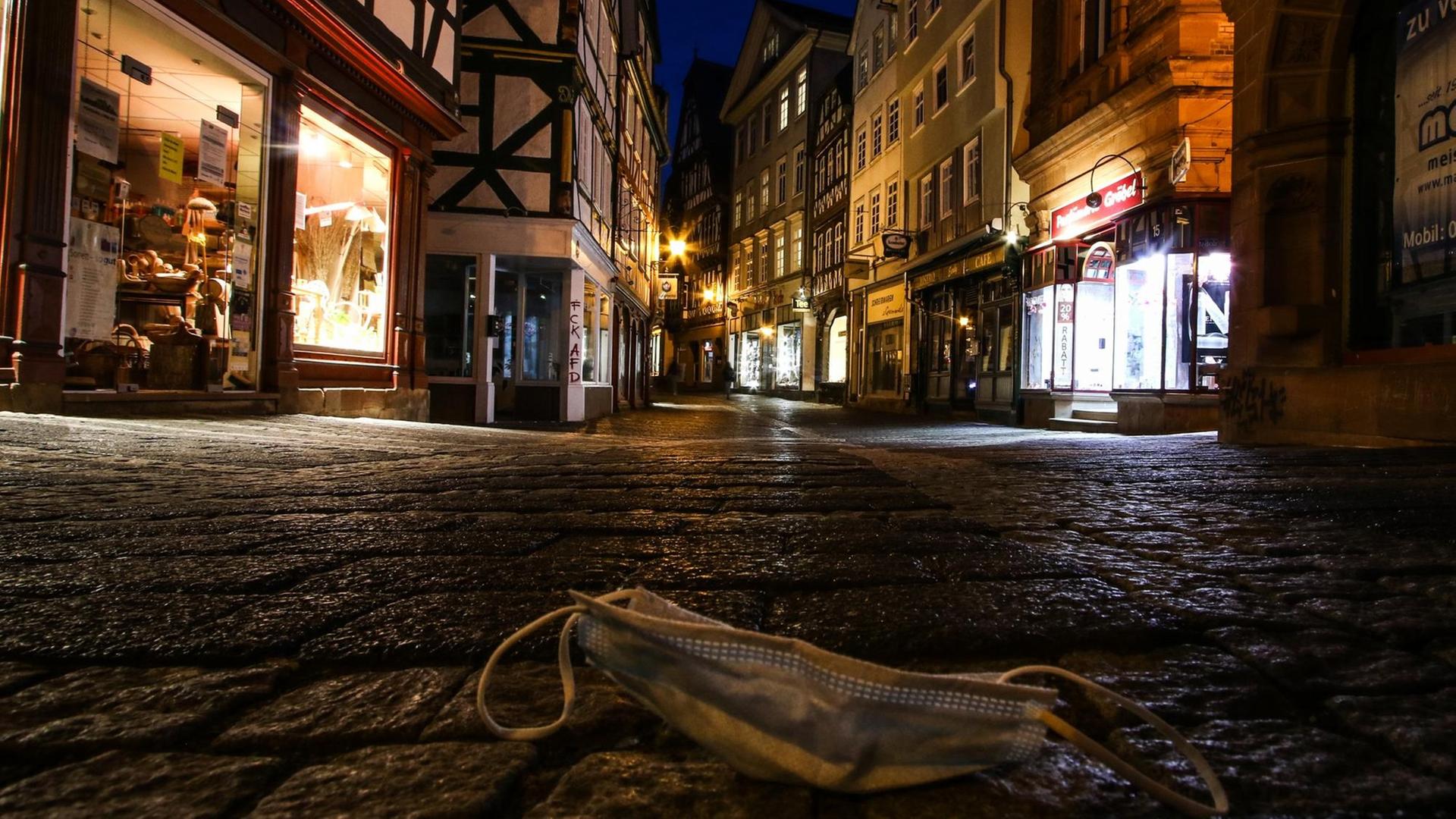 Ein Mund-Nasen-Schutz liegt auf der dunklen, menschenleeren Straße in der in einer gepflasterten Altstadt.
