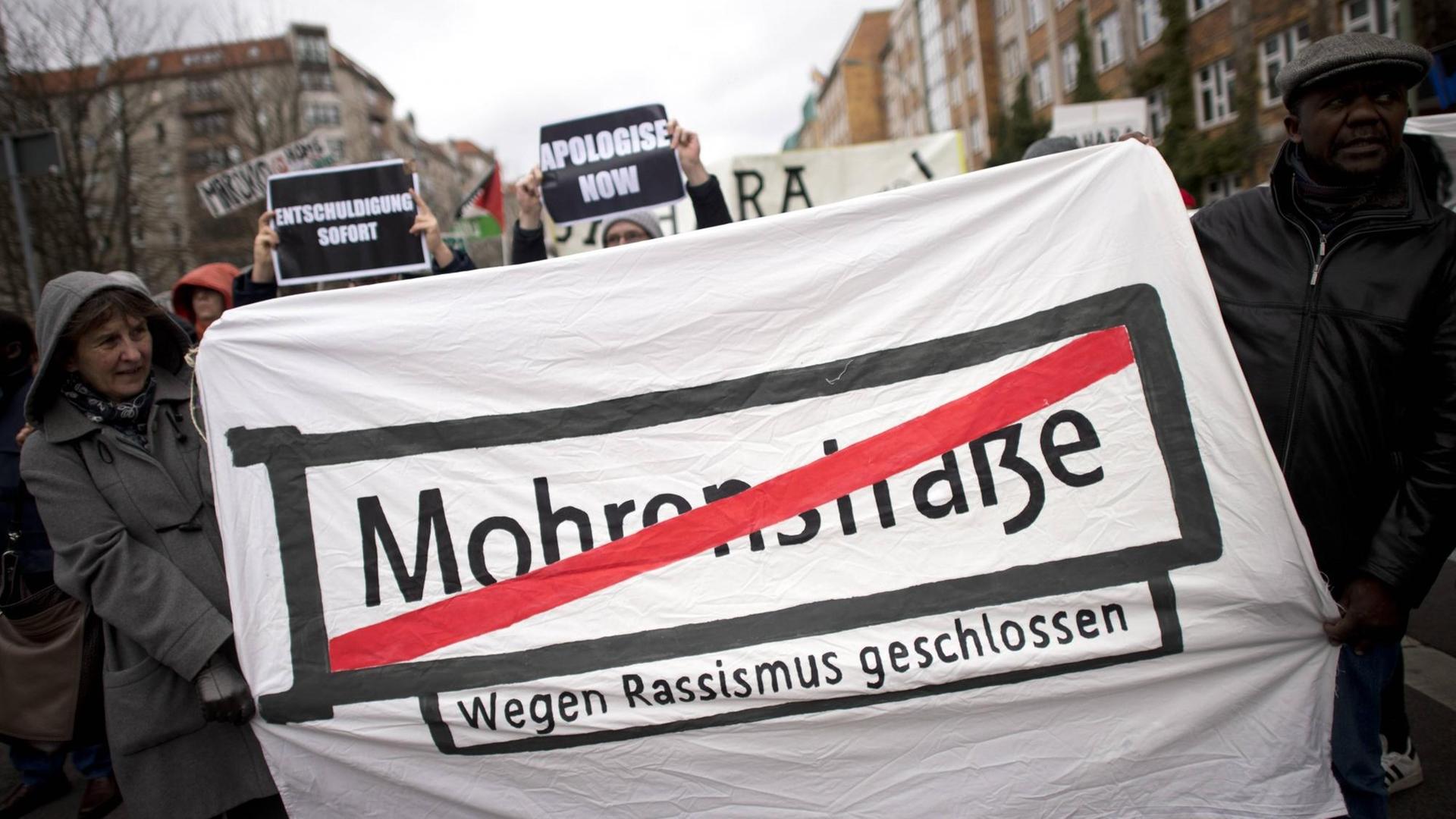 Demonstranten halten ein Transparent mit dem Straßenschild "Mohrenstraße", das rot durchgestrichen wurde.