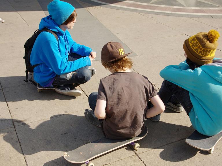 Junge Skateboardfahrer sitzen auf ihren Boards im Sommer 2011 am Alexanderplatz in Berlin.