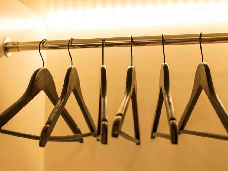 Mehrere leere Kleiderbügel hängen auf einer Kleiderstange und werden angestrahlt.