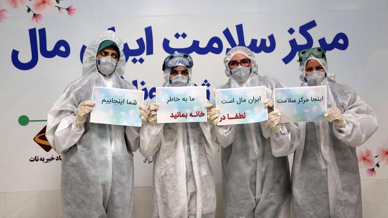Vier Menschen aus der Krankenpflege in Schutzanzügen halten Schilder hoch: "Bitte bleibt zu Hause! Wir sind für Euch da!" 21.März, Teheran, Iran.