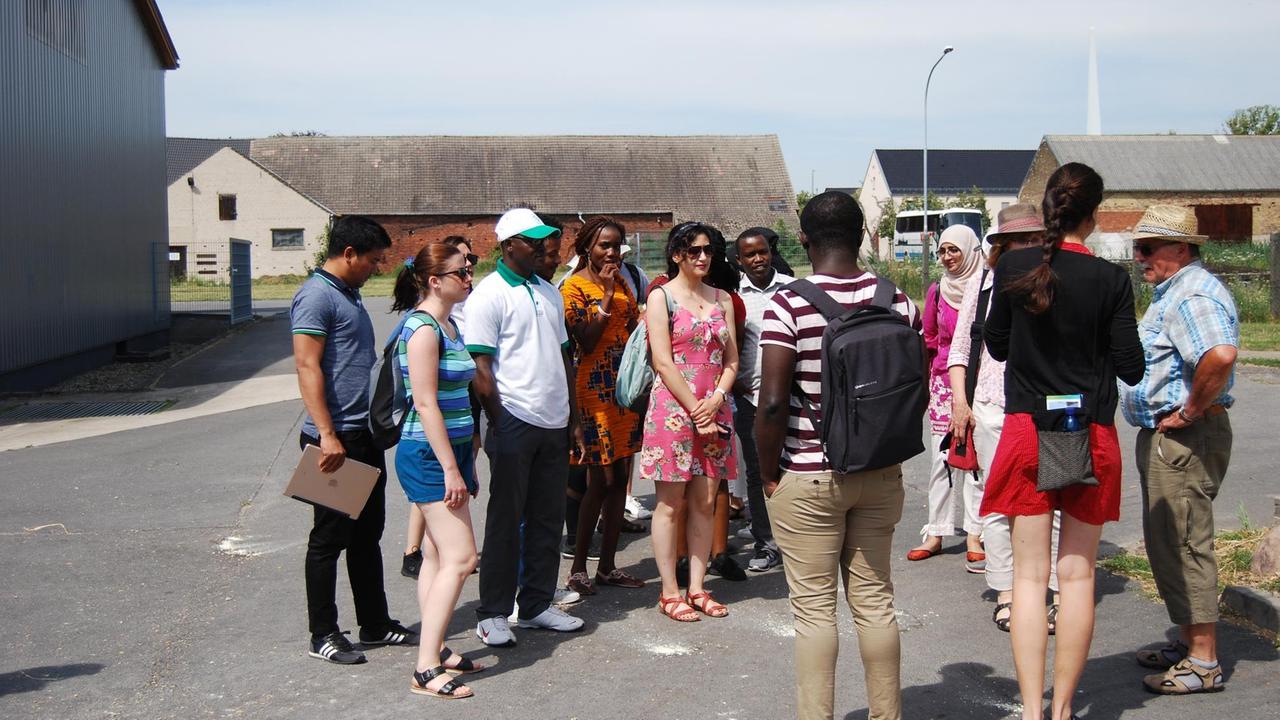 Eine Besuchergruppe in sommerlicher Kleidung steht in Feldheim auf der Straße und hört den Ausführungen von Kathleen Thomson zu.
