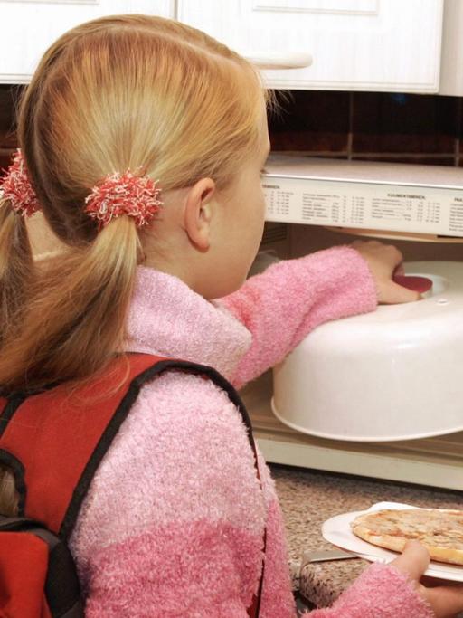 Ein junges Mädchen, das gerade von der Schule nach Haus gekommen ist, wärmt sich in der Mikrowelle etwas zu Essen auf, aufgenommen am 23.11.2004 in Espoo in Finnland.