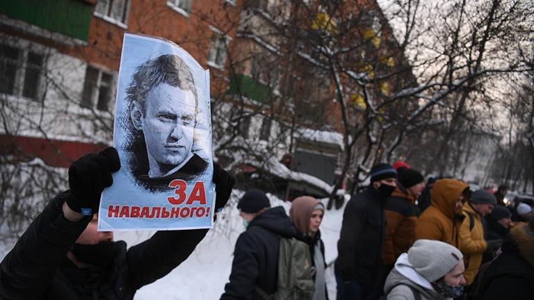 Auf einer verschneiten Straße haben sich Männer, Frauen und Kinder zu einer Protestkundgebung versammelt. Ein Mann hält ein Plakat mit dem Porträt des russischen Oppositionellen Alexej Nawalny hoch.