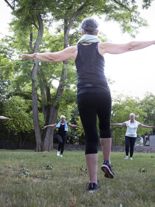 Eine Trainerin leitet im Freien eine Sportgruppe älterer Damen an.