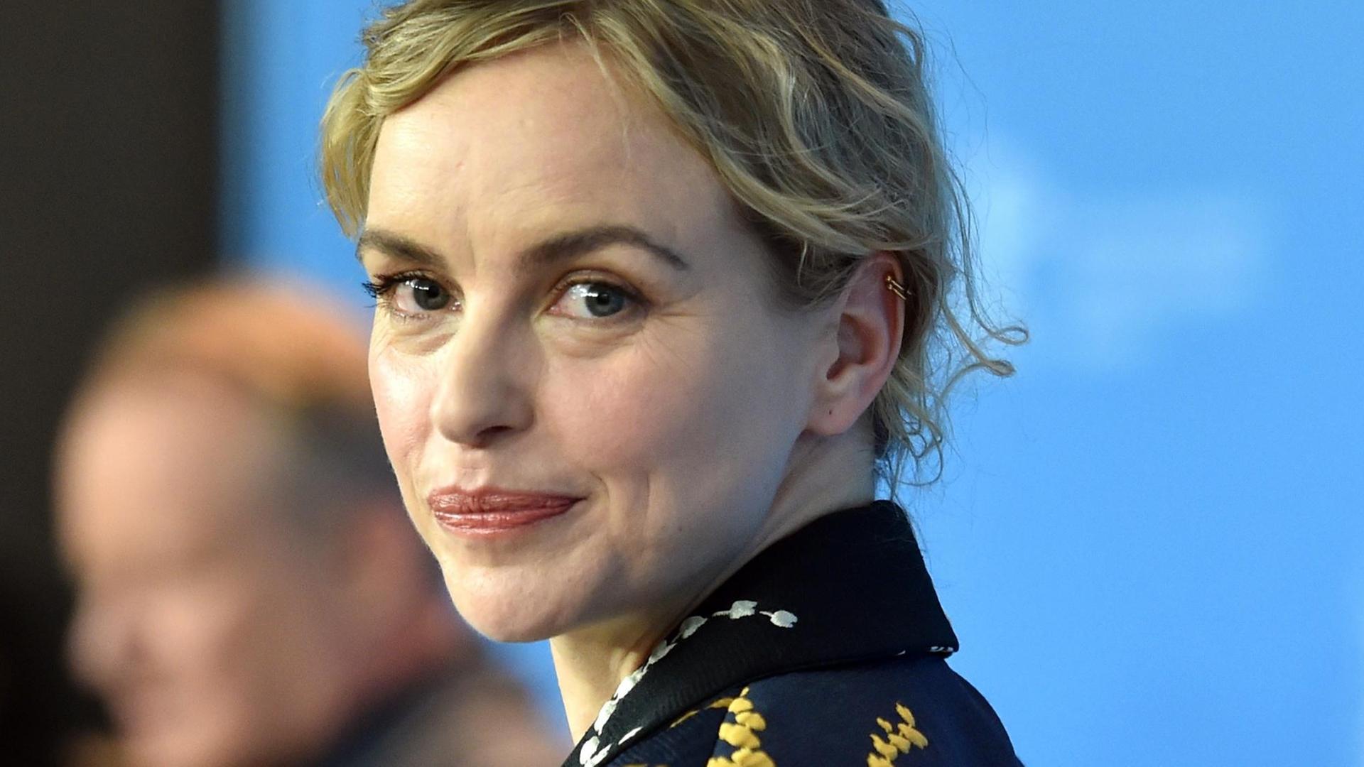 Schauspielerin Nina Hoss blickt über die linke Schulter in die Kamera und lächelt.