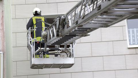 Ein Feuerwehrmann auf einer Hebebühne vor einem Wohnhaus.