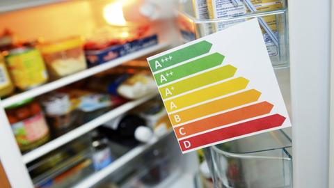 Zettel mit Energieeffizienzklassen vor einem Kühlschrank, dessen Tür aufgeht