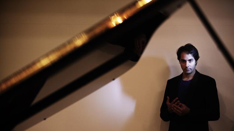 Der Pianist Saleem Ashkar steht in schwarzem Blazer hinter einem aufgeklappten Flügel.
