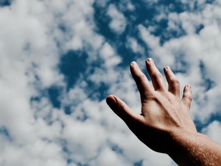 Eine Hand streckt sich dem blauen Himmel mit Schäfchenwölkchen entgegen.