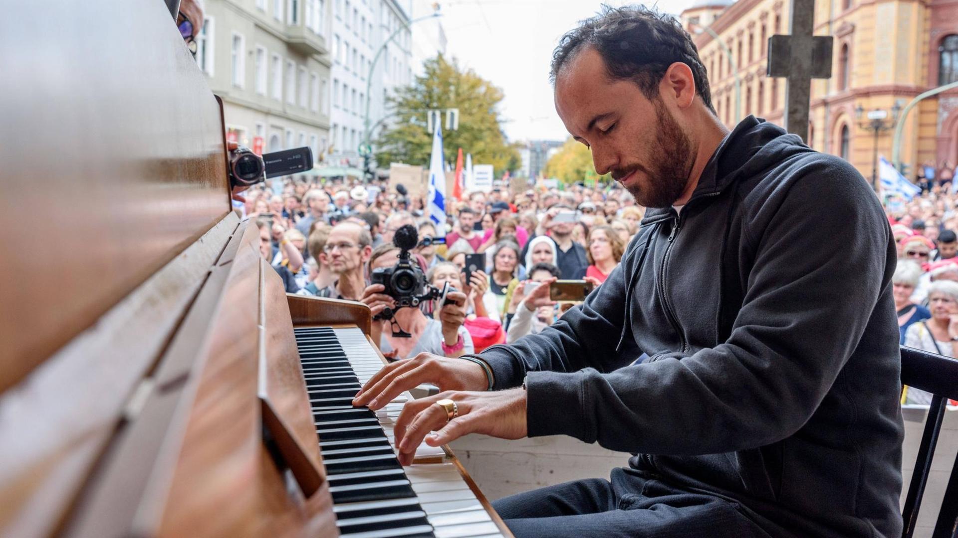 Pianist Igor Levit am Klavier im Freien vor einer Menschenmenge in einer Häuserschlucht.