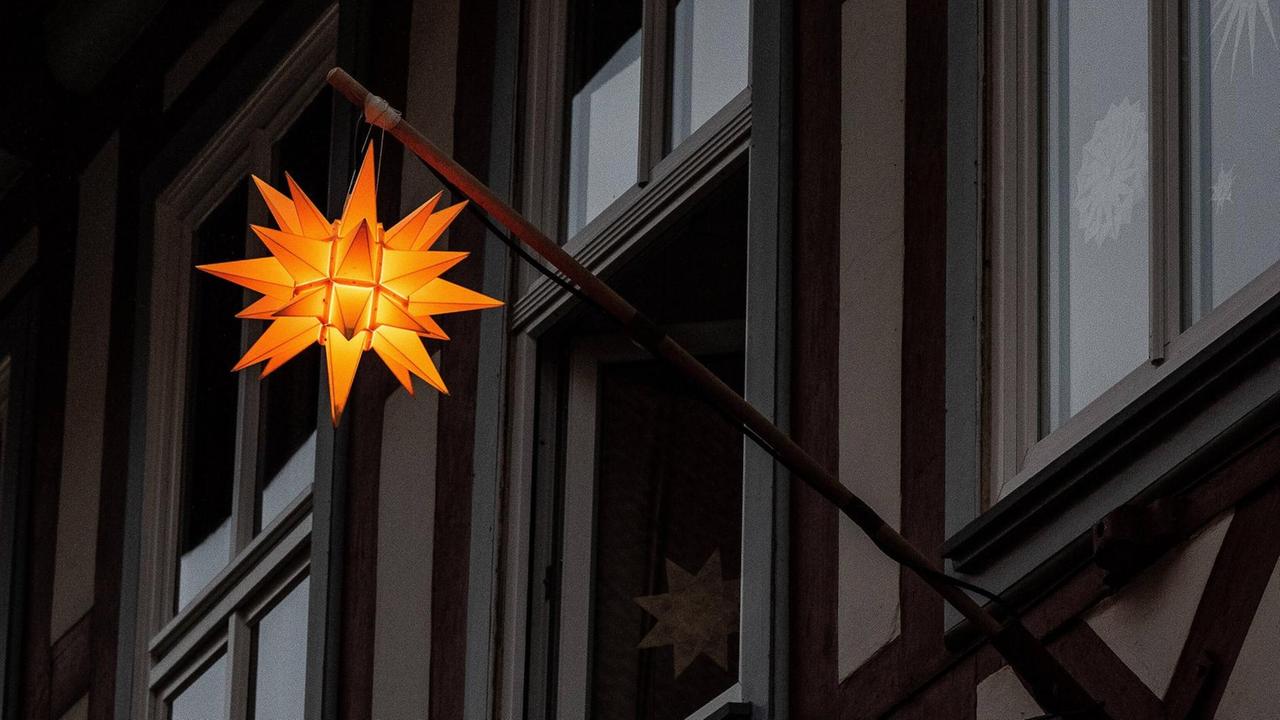 Ein gelber Stern, angebracht an einer Halterung an einem alten Fachwerkhaus, strahlt in die Dunkelheit.