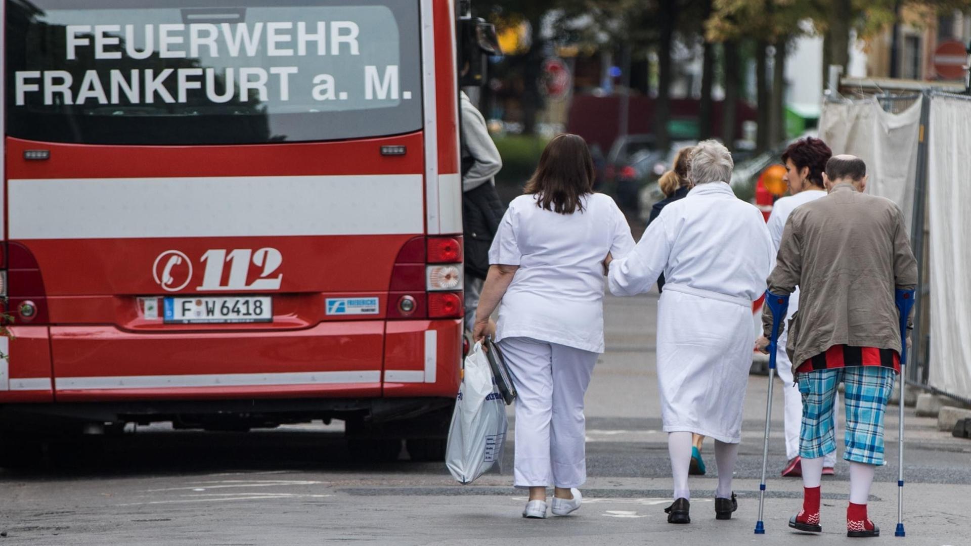 Eine Pflegerin begleitet Patienten zu einem Bus der Feuerwehr Frankfurt am Main.