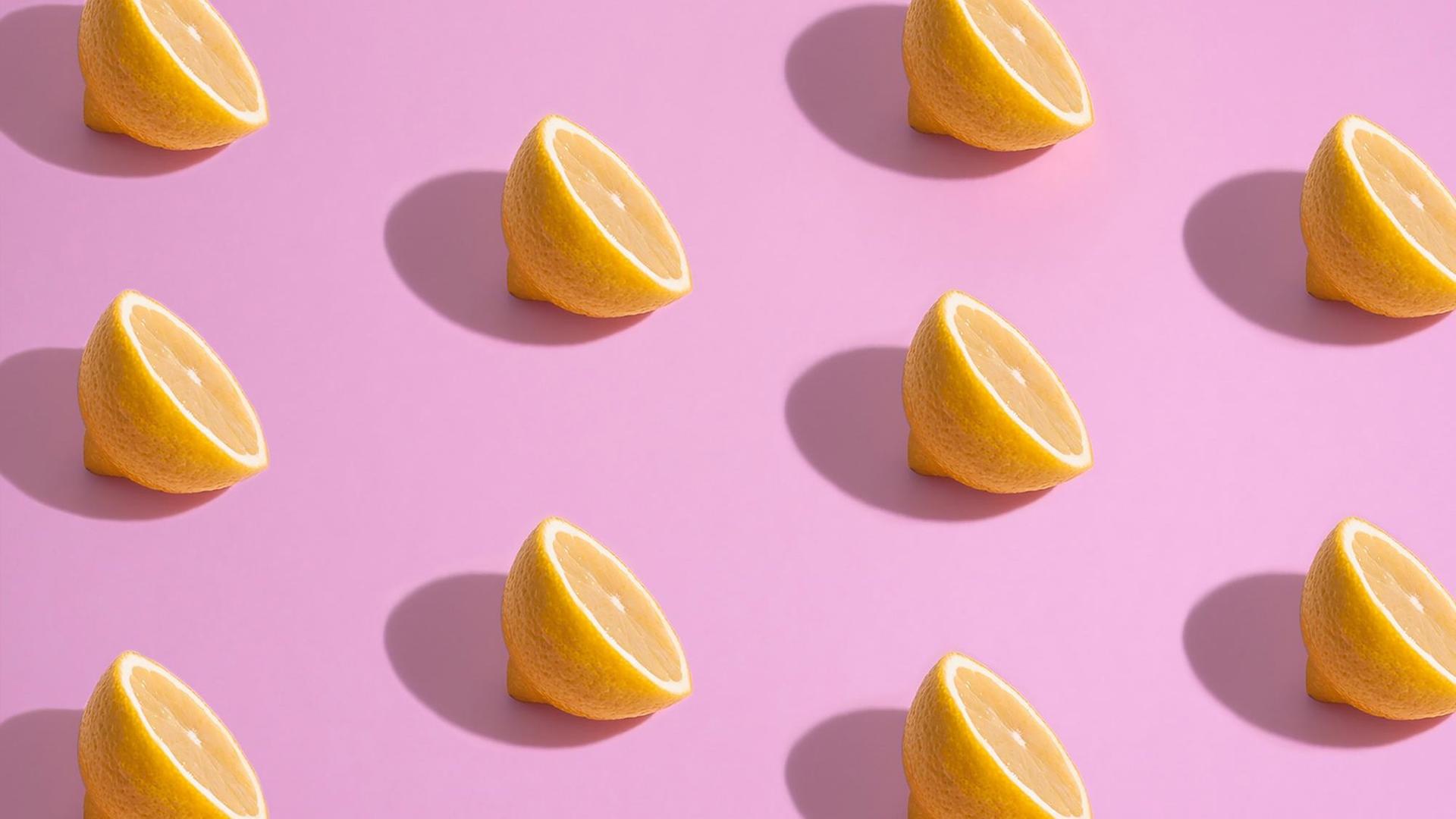 Aufgeschnittene Zitronenhälften liegen auf pinkem Untergrund.