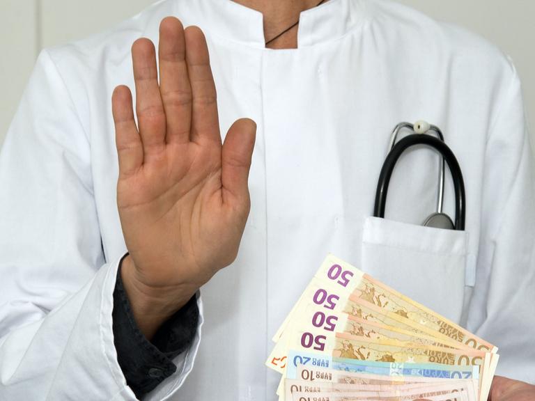 Ein Mann im Arztkittel mit Geldscheinen. Das Symbolfoto steht für Medizin, Geld, Finanzen, Bestechlichkeit, Korruption
