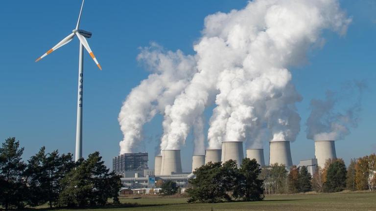 Wasserdampfschwaden steigen aus den Kühltürmen des Braunkohlekraftwerkes der Vattenfall AG in Jänschwalde, daneben steht eine Windenergieanlage (Aufnahme von 2015)