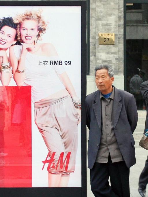 Chinesen und Chinesinnen stehen auf dem Gehweg neben einer Werbung des Modeherstellers H&M.