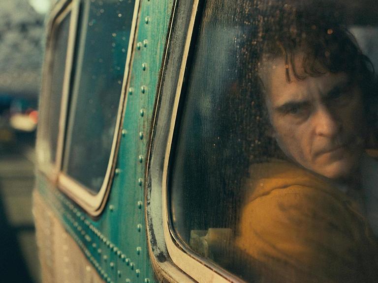Der Schauspieler Joaquin Phoenix in einer Szene des Films "Joker". Er schaut melancholisch aus einem Autofenster auf eine verregnete, nächtliche Straße.