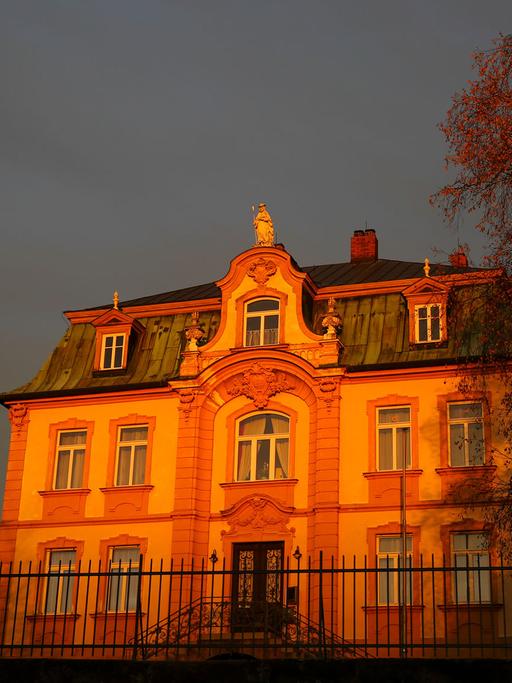 Die untergehende Sonne lässt die Kirche St. Wenzeslaus in Bayern und das zugehörige Pfarrhaus, einen neubarocken Bau im Villenstil orange aufleuchten.