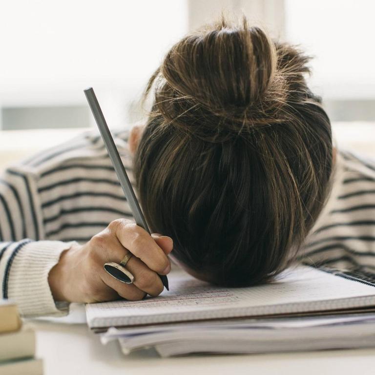 Eine Studentin liegt mit Ihrem Kopf auf einem Arbeitsheft.