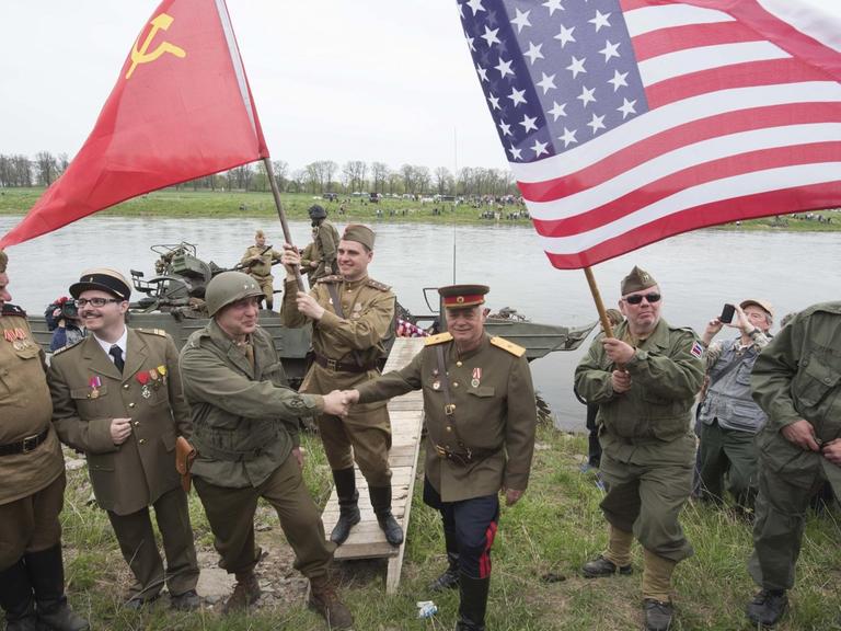 Darsteller amerikanischer und sowjetischer Soldaten reichen sich vor der Elbe die Hand.