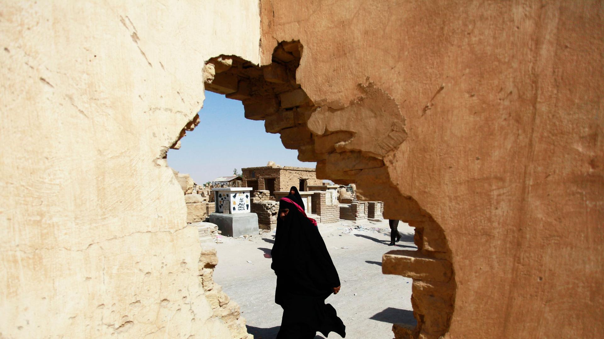 Ein Foto durch ein Loch in einer Mauer zeigt eine schiitische Irakerin, die an Gräbern auf einem der weltgrößten Friedhöfe in der Stadt Najaf vorbeiläuft.