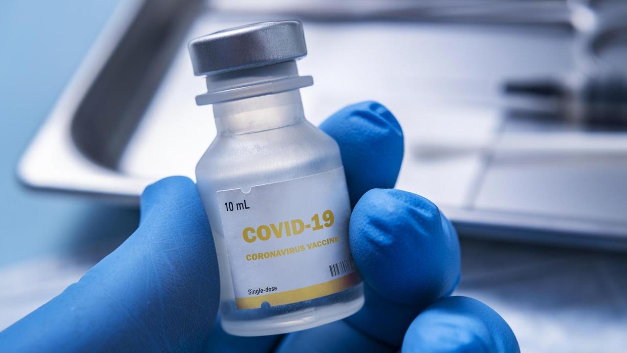 Nahaufnahme einer behandschuhten Hand, die ein Fläschchen mit der Aufschrift "Covid-19 - Coronavirus Vaccine" hält