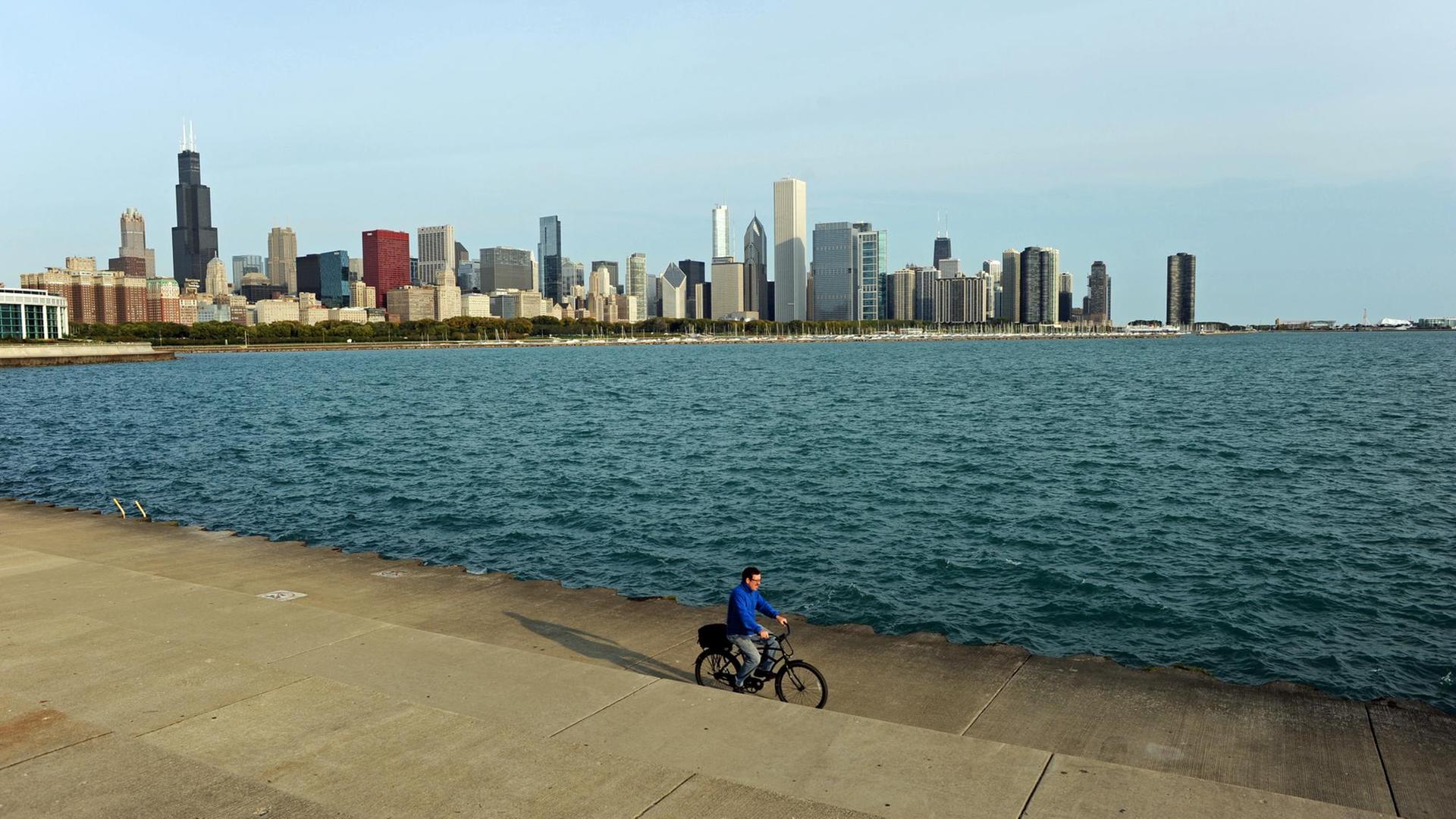 USA: Ein Radfahrer fährt auf der Uferpromenade am Michigansee entlang, dahinter die Skyline von Chicago