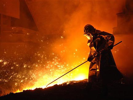 Ein Stahlwerker arbeitet vor einem Hochofen, aus dem Glut und Flammen schlagen
