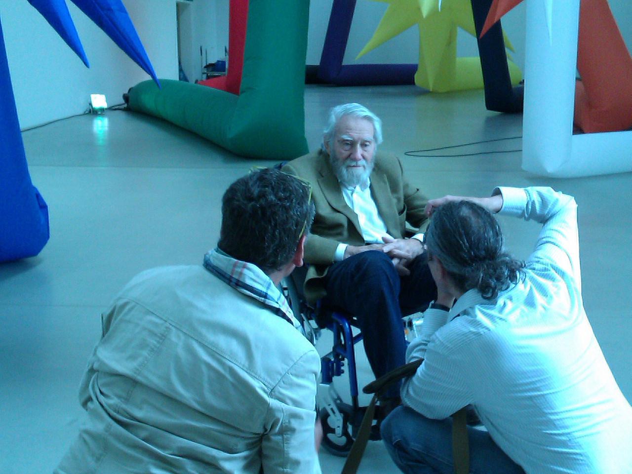 Der Künstler Otto Piene sitzt in einem Stuhl vor seinen Inflatables und wird von zwei Leuten fotografiert.