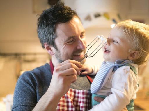 Ein lachender Vater mit kleinem Kind auf dem Arm in der Küche.